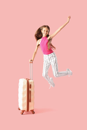Happy little girl with suitcase jumping on pink backgroundの写真素材