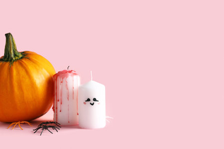 Composition with different candles, pumpkin and spiders for Halloween celebration on pink backgroundの写真素材