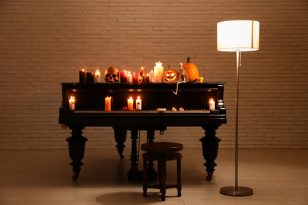 Grand piano with burning candles, lamp, stool and Halloween decor in dark roomの写真素材
