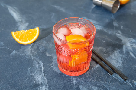 Glass of cold Negroni cocktail and straws on color background