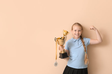 Cute little schoolgirl with gold cups and medal on beige backgroundの写真素材
