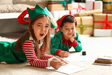 Cute little children dressed as elves writing letters to Santa at home on Christmas Eveの写真素材