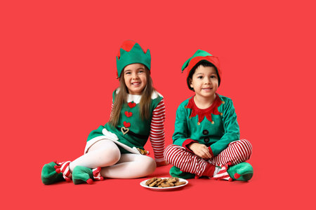Cute little dressed children as elves with cookies on red backgroundの写真素材