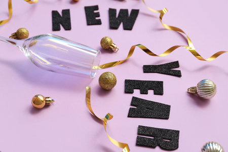Text NEW YEAR with Christmas balls and glass on lilac backgroundの写真素材