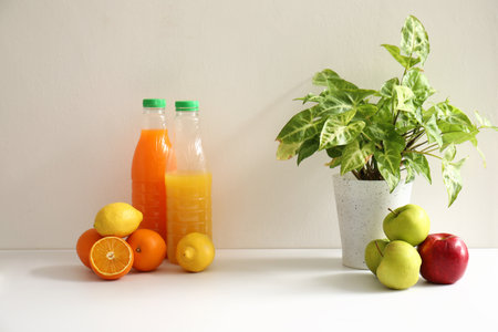 Bottles of juice, fresh fruits and houseplant on white kitchen counterの写真素材