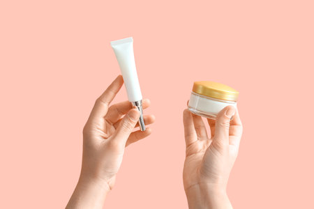 Female hands holding cosmetic cream bottle and jar on pink backgroundの写真素材