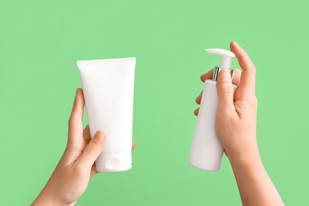 Female hands holding white tube and bottle of cosmetic products on green backgroundの写真素材