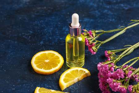 Bottle of cosmetic oil with beautiful flowers and lemon on blue background