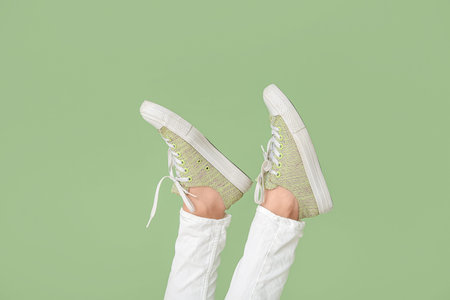 Female legs in stylish gumshoes on green background