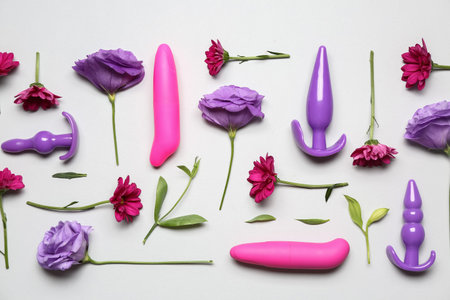 Different sex toys and beautiful flowers on light background