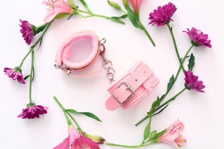 Pink handcuffs from sex shop and beautiful flowers on white background