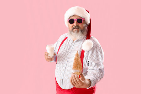 Santa Claus with decorative Christmas tree and glass of milk on pink backgroundの写真素材