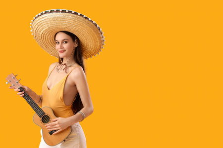 Beautiful woman in sombrero hat and with guitar on yellow backgroundの写真素材