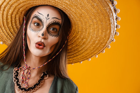 Young woman with painted skull on her face for Mexico's Day of the Dead against yellow backgroundの写真素材