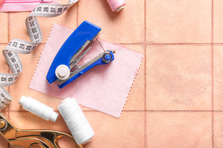 Manual sewing machine with different supplies on pink tile background