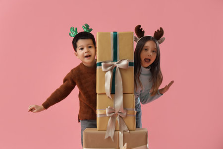 Cute little children with Christmas gifts on pink backgroundの写真素材