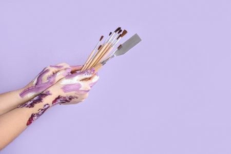 Female hands with artist's brushes and palette knife on lilac backgroundの写真素材