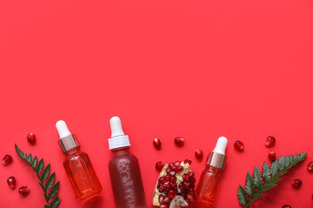 Composition with bottles of essential oil, fern leaves and pomegranate on red backgroundの写真素材