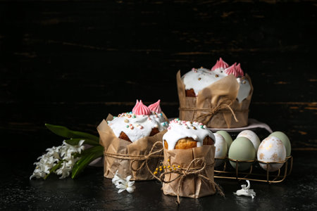 Sweet Easter cakes, beautiful flowers and holder with eggs on black background