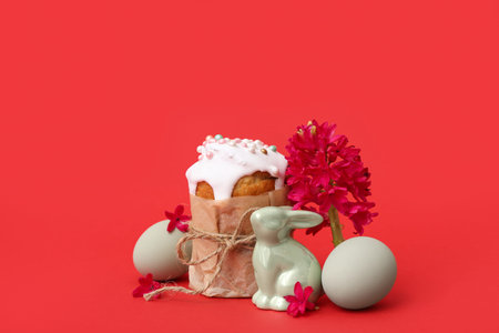 Beautiful composition of Easter cake, painted eggs, hyacinth and bunny on red background