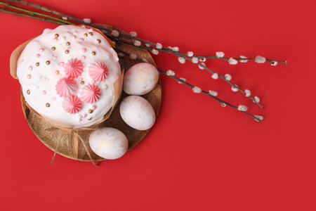 Easter cake, painted eggs on wooden tray and willow branches on red background