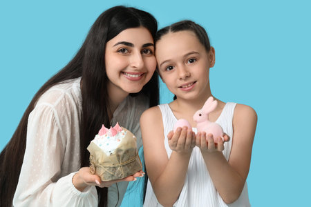Happy smiling young woman and her daughter with Easter cake and toy bunny on blue backgroundの写真素材