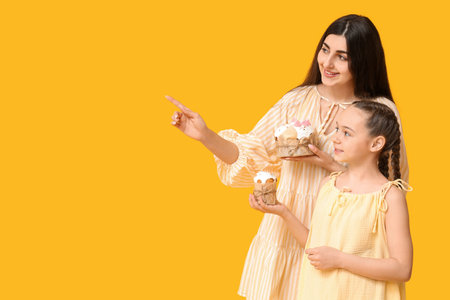 Happy smiling young woman and her daughter with Easter cakes pointing at something on orange backgroundの写真素材