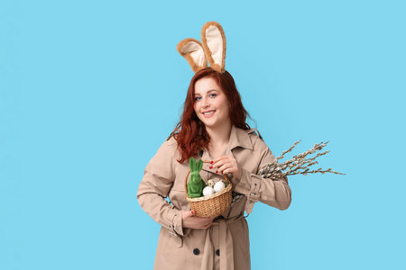 Beautiful young woman in bunny ears with pussy willow branches and Easter basket on blue backgroundの写真素材