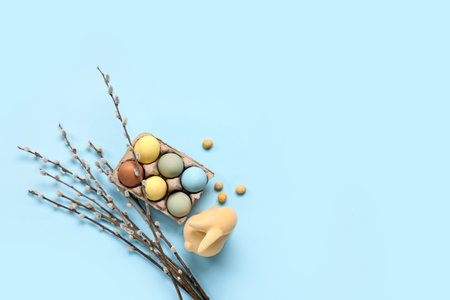 Holder with Easter eggs, pussy willow branches and toy bunny on blue backgroundの写真素材