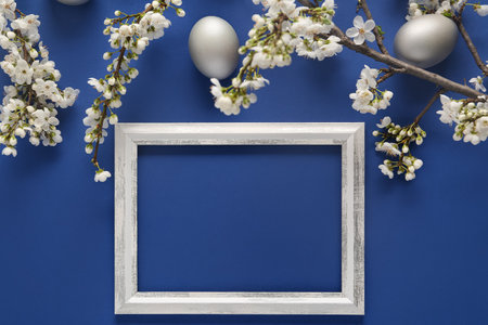Frame with silver Easter eggs and blossoming branches on blue backgroundの写真素材