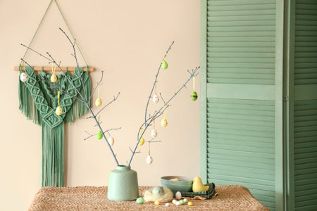 Vase with tree branches and Easter eggs on table in stylish room