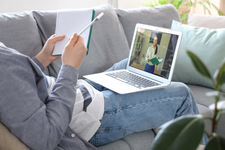 Male student with notebook and laptop studying online on sofa at home, closeupの写真素材