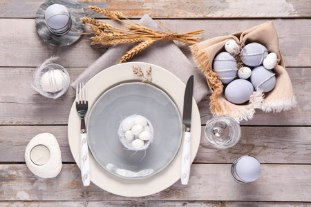 Stylish table setting for Easter celebration with painted eggs on gray wooden background. Top view
