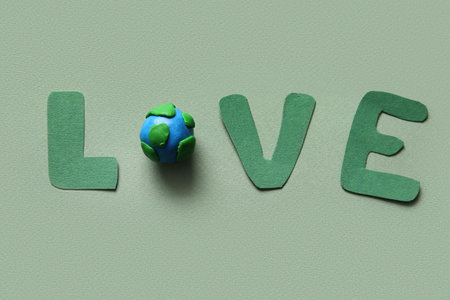 Word LOVE made of felt letters and plasticine planet Earth on green background, closeup. Earth Day...