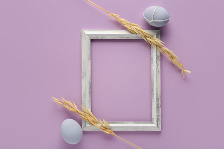 Beautiful composition with frame, Easter eggs and ears of wheat on color backgroundの写真素材