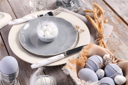 Stylish table setting for Easter celebration with painted eggs on gray wooden background