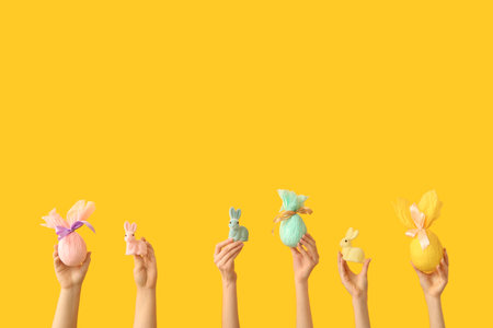 Female hands with Easter bunnies and gift eggs on yellow backgroundの写真素材