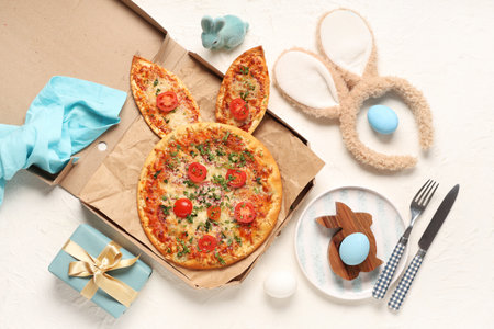 Cardboard box of Easter pizza with bunny ears, painted eggs and gift on white backgroundの写真素材