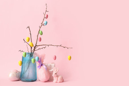 Branches with Easter eggs in glass vase, rabbit and gift egg on pink background