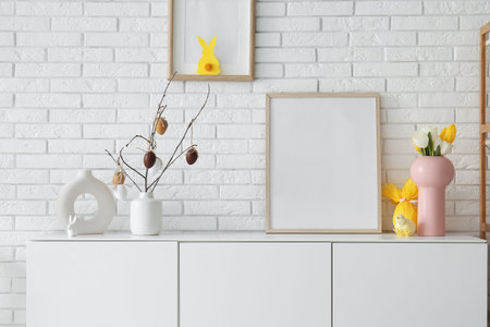 Photo frame and Easter decor on chest of drawers near white brick wall