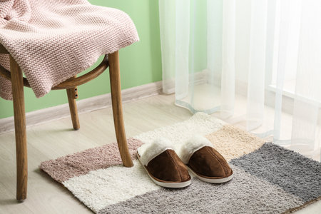 Pair of brown soft slippers near chair on carpet in roomの写真素材