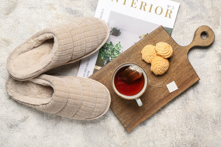 Pair of soft beige slippers with cup of tea and cookies on gray grunge background. Top viewの写真素材