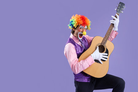 Portrait of clown playing guitar on lilac background. April Fool's day celebrationの写真素材