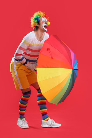 Portrait of clown with colorful umbrella on red background. April Fool's day celebrationの写真素材
