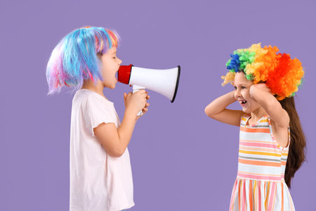 Little brother and sister with colorful wigs and megaphone on lilac background. April Fool's Day celebrationの写真素材