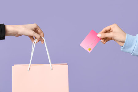 Female hands with shopping bag and credit card on lilac backgroundの写真素材