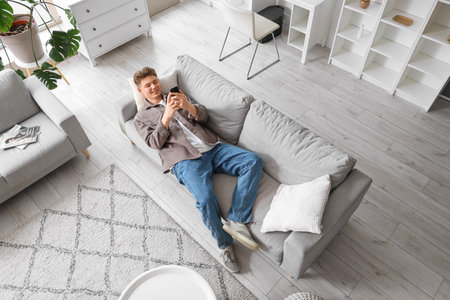 Young man using mobile phone on sofa at home, top viewの写真素材
