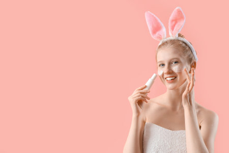 Young woman after shower with bunny ears and cosmetic product on pink backgroundの写真素材