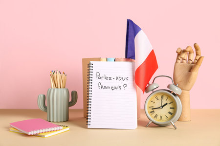 Notebook with French phrase, flag, stationery and alarm clock on table against color backgroundの写真素材