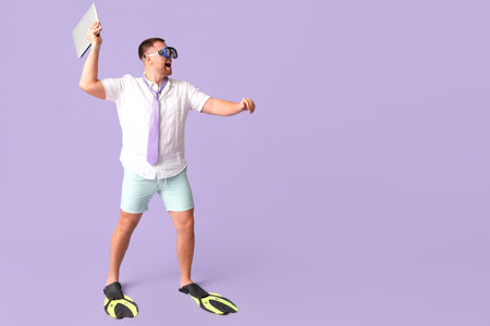Happy office worker in diving mask and flippers throws laptop on lilac backgroundの写真素材